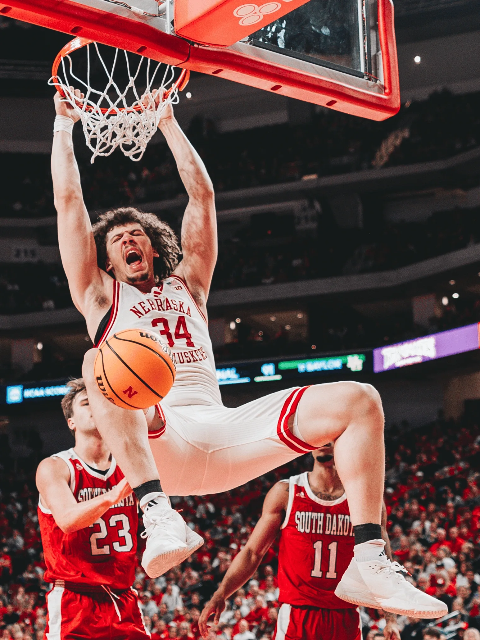 Nebraska center Braxton Meah hangs on the rim after throwing down a dunk over South Dakota defenders during a men's basketball game at Pinnacle Bank Arena in Lincoln, Neb. The 7-foot-1 transfer from Washington scored 12 points, all on dunks, as the Cornhuskers defeated the Coyotes 96-79 on Nov. 27, 2024.