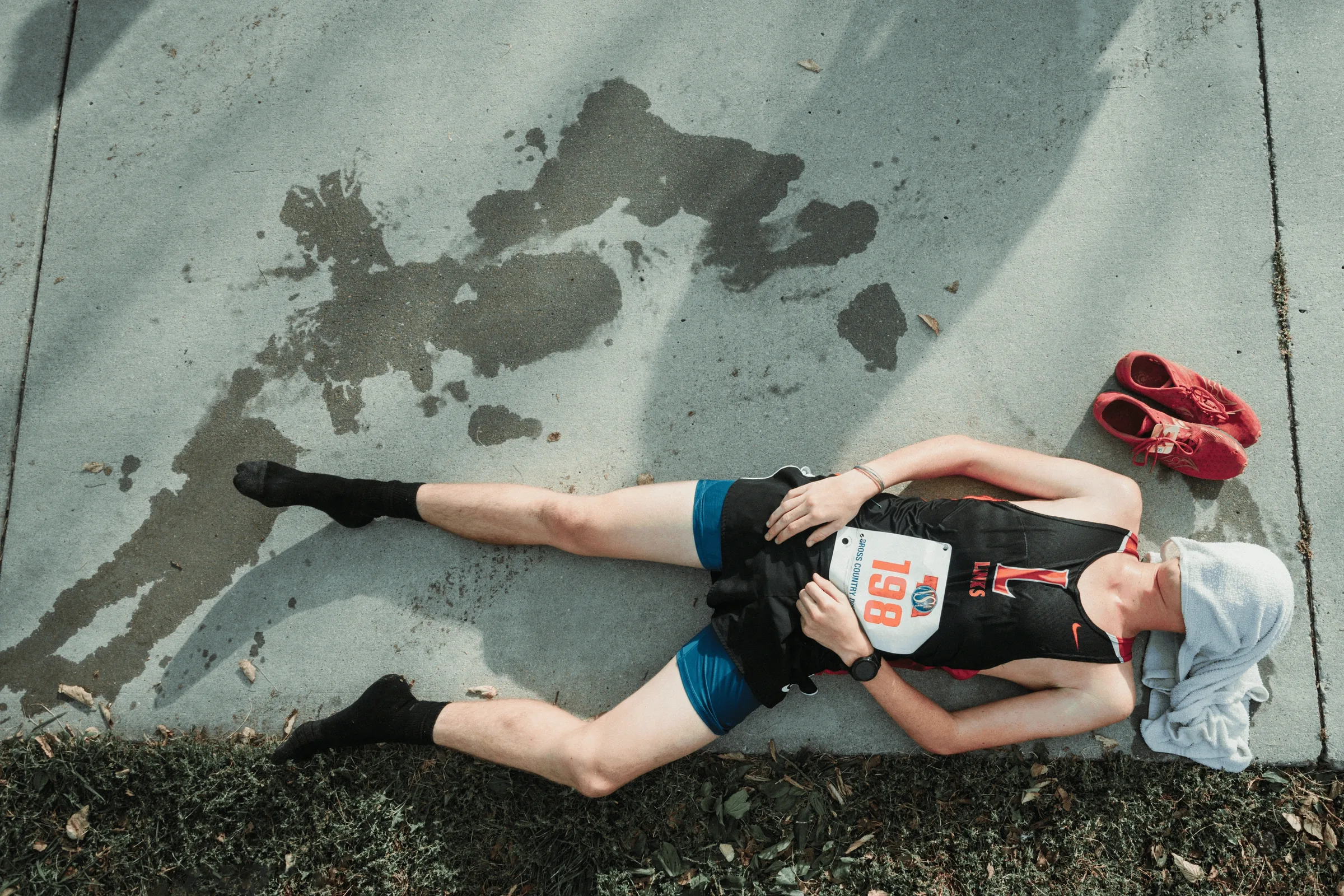 Lincoln High cross country runner Trey Crabtree lies on the concrete after finishing the 5K race, his shoes cast aside beside him. Crabtree's effort helped the Links qualify for the Nebraska state cross country championships as a team for the first time in more than a decade.