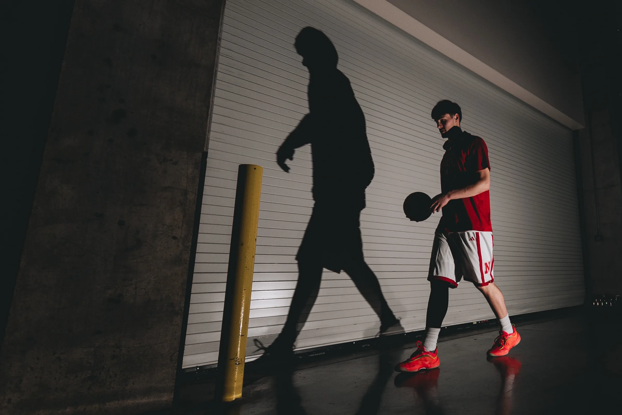 Nebraska Cornhuskers freshman forward Braden Frager dribbles a basketball as his shadow is cast across a tunnel wall at Pinnacle Bank Arena in Lincoln, Nebraska, on Sunday, Dec. 7, 2025. Nebraska defeated Creighton 71-50, extending the Cornhuskers' unbeaten record to 9-0 with their 13th consecutive victory.